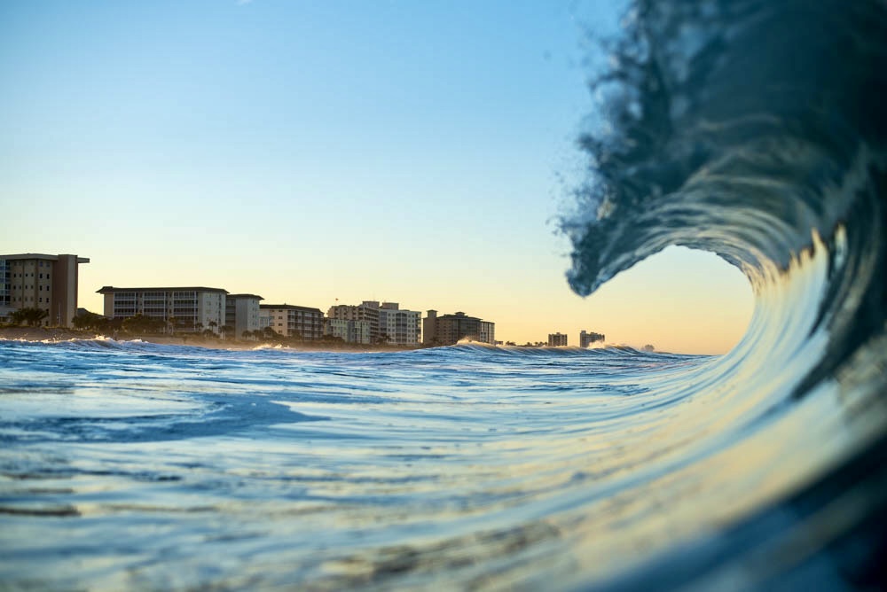 View from inside a curling wave, with coastal buildings along the shoreline